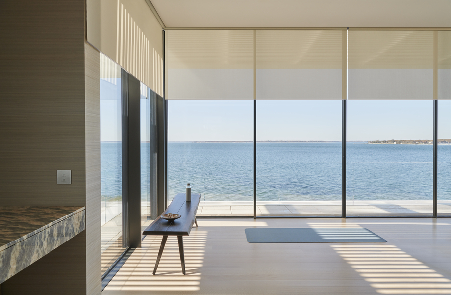 Motorized Lutron shades partially lowered over floor-to-ceiling windows in a modern waterfront home with ocean views.  Social Media Bl