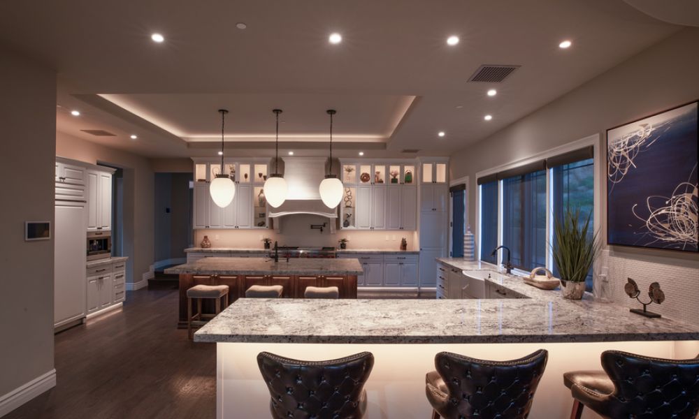 High-end kitchen featuring a large granite island with backlit paneling, pendant lighting, dark wood flooring, and white cabinetry.