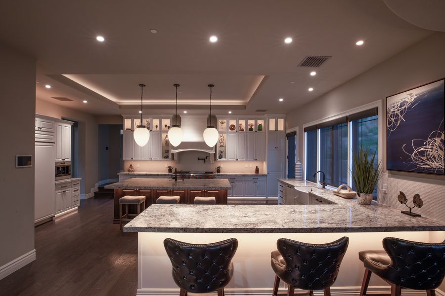 High-end kitchen featuring a large granite island with backlit paneling, pendant lighting, dark wood flooring, and white cabinetry.